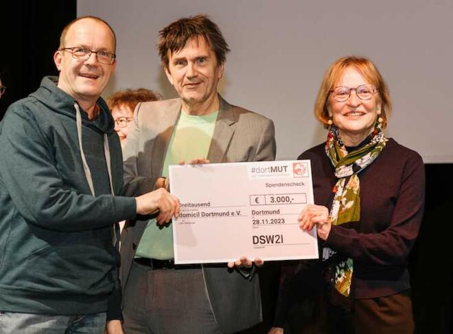 Das Bild zeigt drei Personen, die einen überdimensionalen Scheck in die Kamera halten.